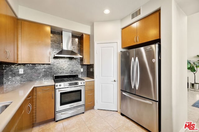 kitchen with appliances with stainless steel finishes, wall chimney range hood, light tile patterned floors, and decorative backsplash