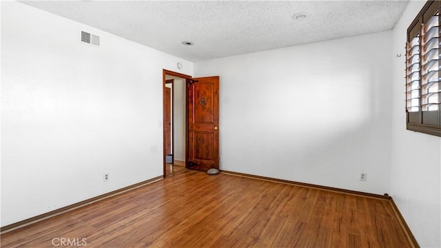 spare room with a textured ceiling, wood finished floors, visible vents, and baseboards