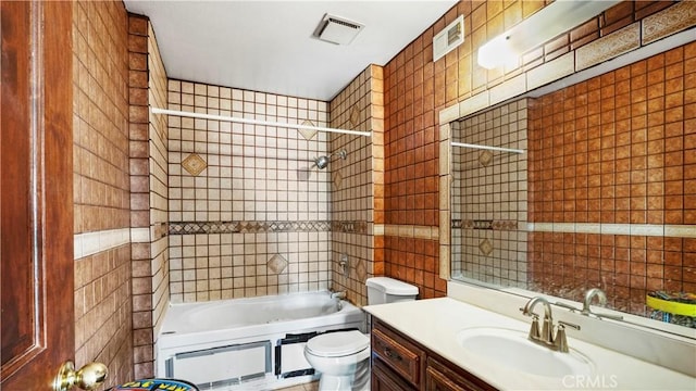 full bath featuring toilet, visible vents, vanity, tile walls, and washtub / shower combination