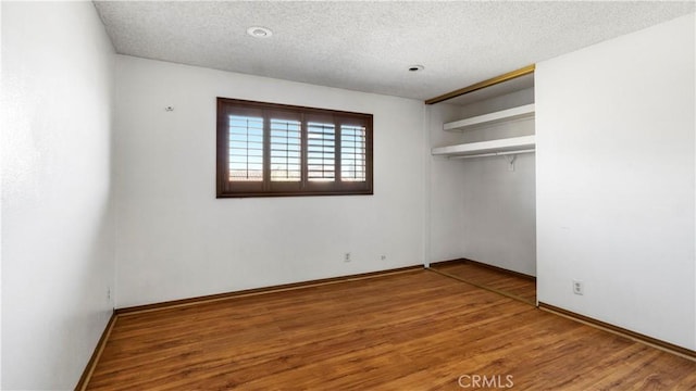 unfurnished bedroom featuring a closet, a textured ceiling, baseboards, and wood finished floors