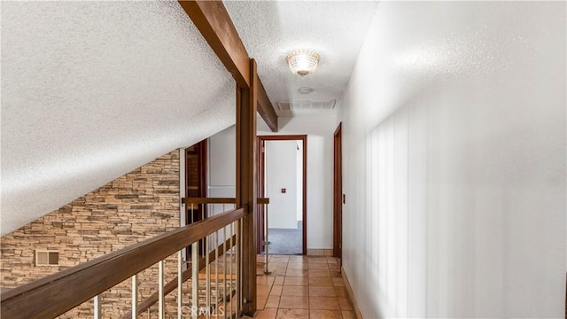 hallway with a textured ceiling, light tile patterned floors, lofted ceiling, visible vents, and an upstairs landing