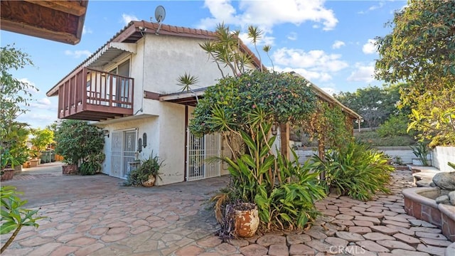 rear view of house with a balcony, a tiled roof, a patio, and stucco siding