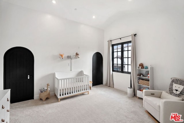 carpeted bedroom with a crib and vaulted ceiling