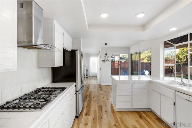 kitchen with a raised ceiling, white cabinetry, appliances with stainless steel finishes, and wall chimney exhaust hood