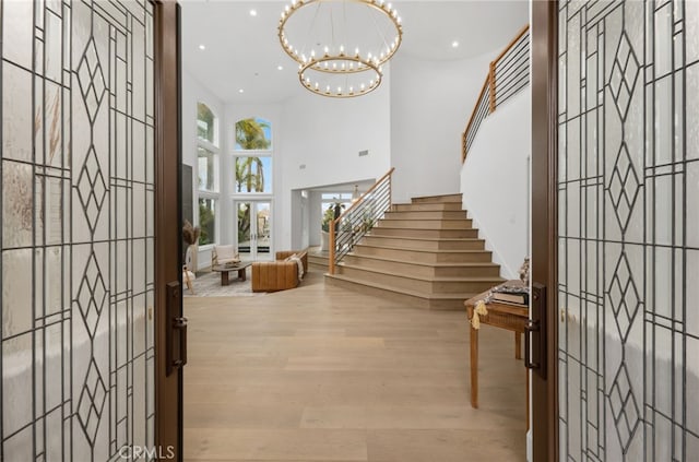 entrance foyer with recessed lighting, a notable chandelier, wood finished floors, a towering ceiling, and stairway