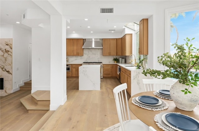 kitchen with visible vents, backsplash, light wood-style floors, a sink, and wall chimney range hood