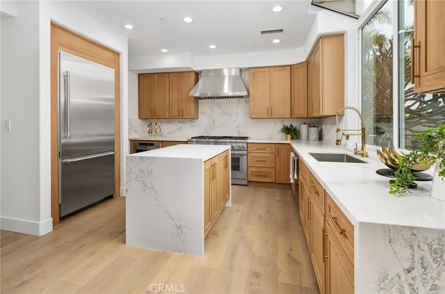 kitchen featuring light wood finished floors, a kitchen island, a sink, wall chimney range hood, and high quality appliances