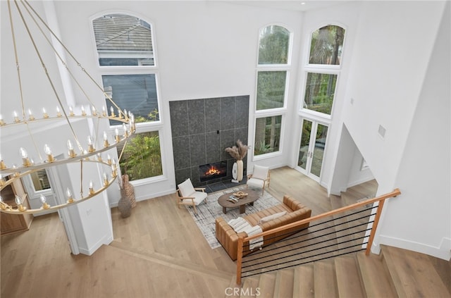 living room with a tiled fireplace, wood finished floors, a towering ceiling, and baseboards