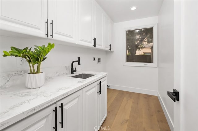 laundry area with cabinet space, light wood-style flooring, a sink, electric dryer hookup, and baseboards