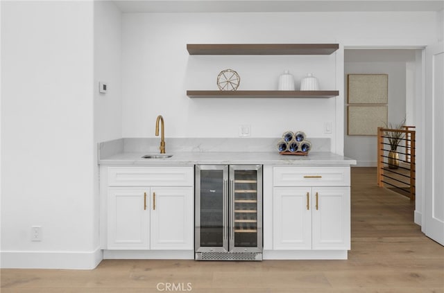 bar with light wood finished floors, baseboards, wine cooler, wet bar, and a sink