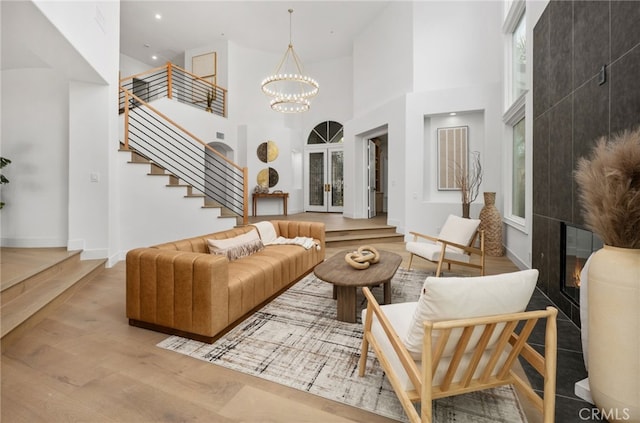 living area featuring a tile fireplace, a high ceiling, wood finished floors, stairway, and an inviting chandelier