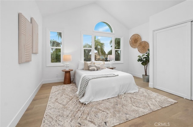 bedroom with high vaulted ceiling, multiple windows, light wood-style flooring, and baseboards