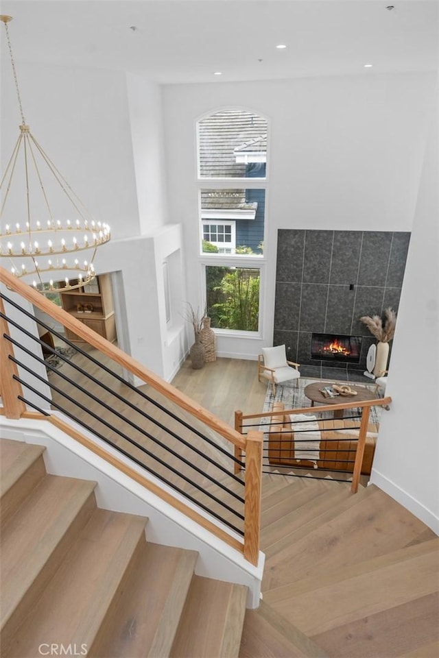 stairway with baseboards, a tiled fireplace, wood finished floors, a notable chandelier, and recessed lighting