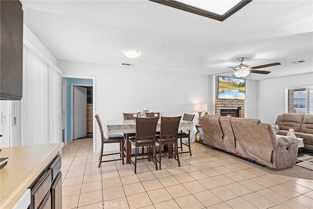 tiled dining room featuring a textured ceiling, a fireplace, and ceiling fan