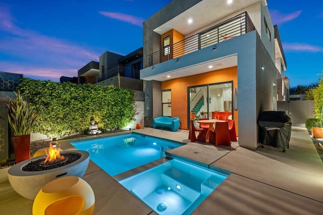 pool at dusk featuring an in ground hot tub, a patio area, and an outdoor fire pit