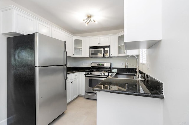 kitchen featuring appliances with stainless steel finishes, white cabinetry, sink, dark stone countertops, and kitchen peninsula