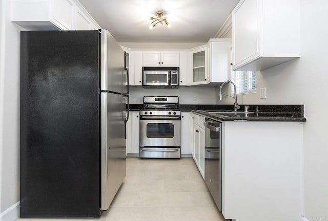 kitchen with sink, stainless steel appliances, dark stone counters, and white cabinets