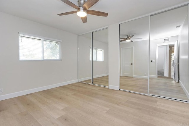 unfurnished bedroom featuring multiple closets, ceiling fan, and light hardwood / wood-style flooring