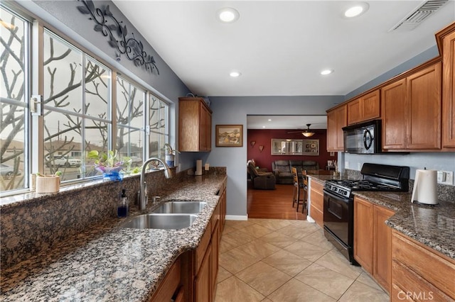 kitchen with sink, light tile patterned floors, ceiling fan, dark stone countertops, and black appliances