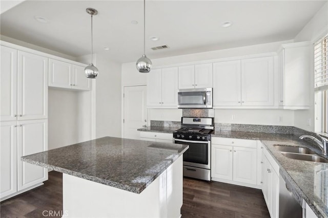 kitchen featuring appliances with stainless steel finishes, decorative light fixtures, sink, white cabinets, and a center island