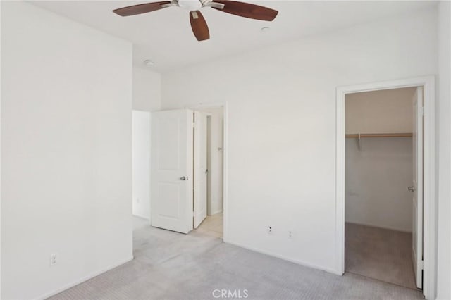 unfurnished bedroom with a spacious closet, light colored carpet, a closet, and ceiling fan