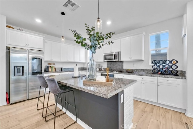 kitchen featuring appliances with stainless steel finishes, decorative light fixtures, white cabinets, a kitchen island with sink, and light stone countertops