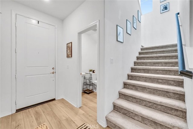 foyer featuring light wood finished floors, baseboards, and stairway