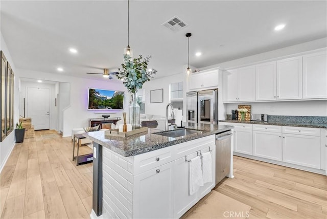 kitchen with sink, a kitchen island with sink, hanging light fixtures, stainless steel appliances, and white cabinets