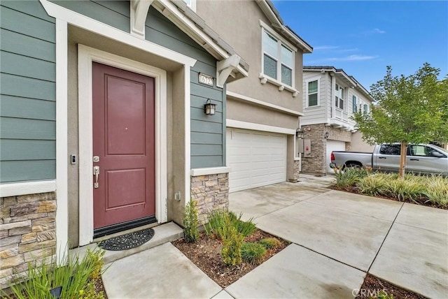 entrance to property featuring a garage, driveway, and stone siding