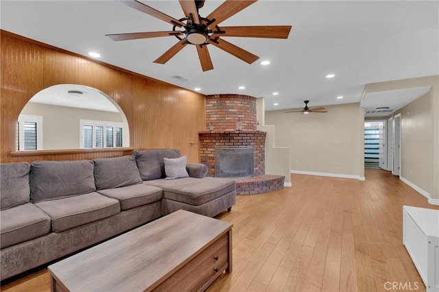 living room featuring a brick fireplace, light hardwood / wood-style floors, ceiling fan, and wood walls