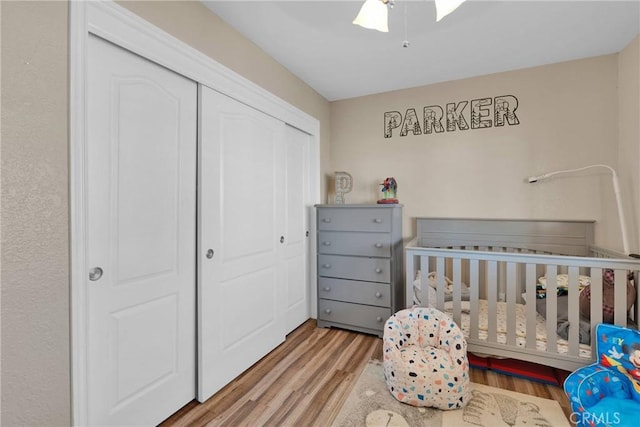 bedroom with a nursery area, ceiling fan, a closet, and light hardwood / wood-style flooring