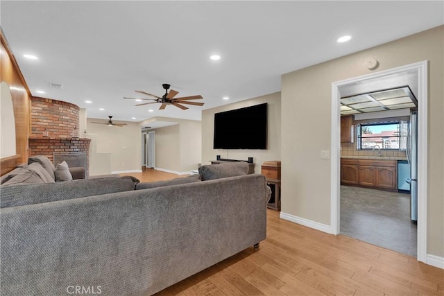 living room with ceiling fan, sink, and light wood-type flooring