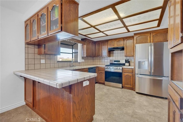 kitchen with tasteful backsplash, appliances with stainless steel finishes, tile counters, and kitchen peninsula