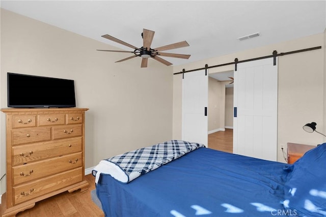 bedroom featuring wood-type flooring, a barn door, and ceiling fan