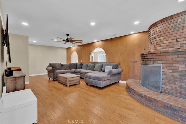 living room with a fireplace, wooden walls, ceiling fan, and light wood-type flooring