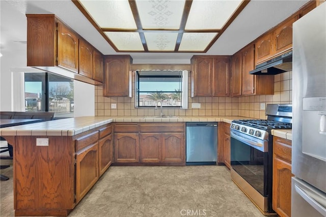 kitchen with sink, tasteful backsplash, tile countertops, kitchen peninsula, and stainless steel appliances