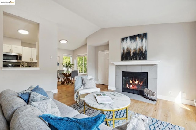 living room featuring a fireplace, light hardwood / wood-style floors, and vaulted ceiling