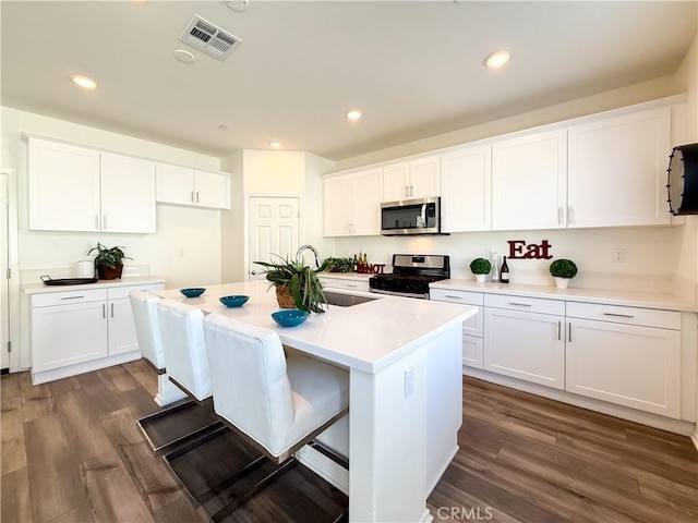 kitchen featuring white cabinetry, stainless steel appliances, dark hardwood / wood-style floors, and a kitchen island with sink