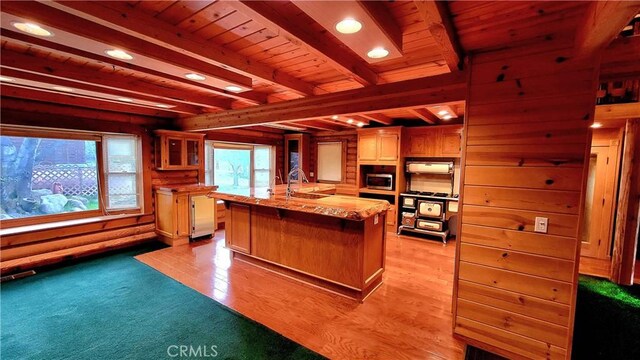 kitchen featuring sink, wood ceiling, a kitchen island with sink, beam ceiling, and stainless steel microwave