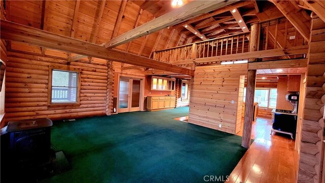 unfurnished living room with high vaulted ceiling, wood-type flooring, rustic walls, wooden ceiling, and beam ceiling