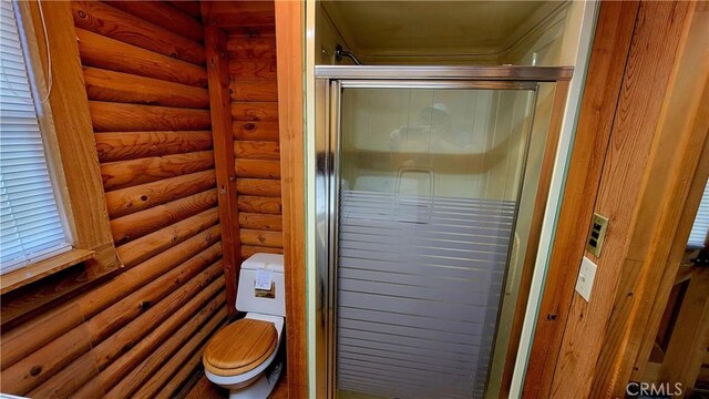 bathroom featuring toilet, a shower with shower door, and log walls