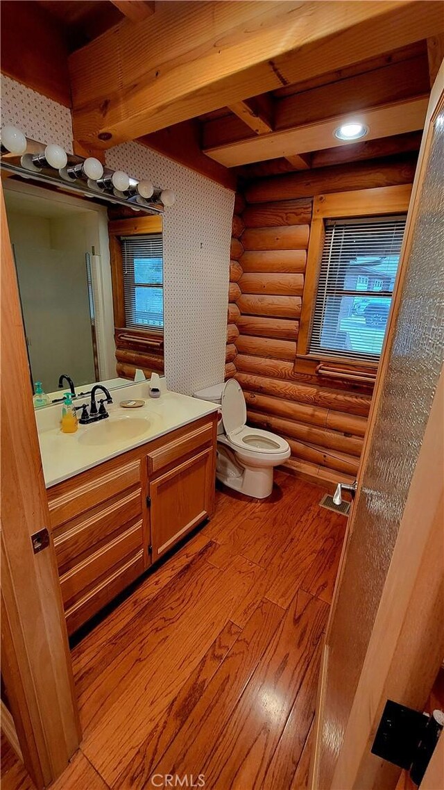 bathroom with vanity, log walls, wood-type flooring, and toilet