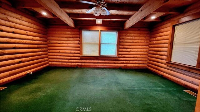 carpeted spare room with beamed ceiling, ceiling fan, and rustic walls