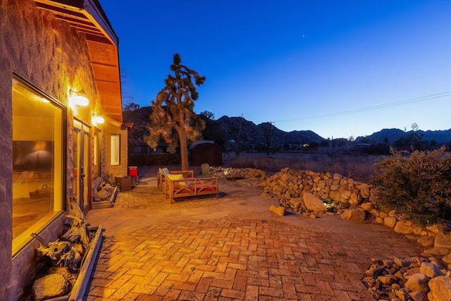 patio terrace at dusk featuring a mountain view and a storage unit