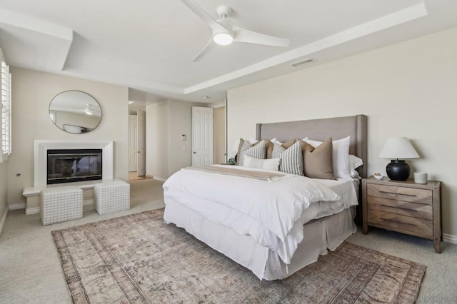 carpeted bedroom with ceiling fan and a tray ceiling