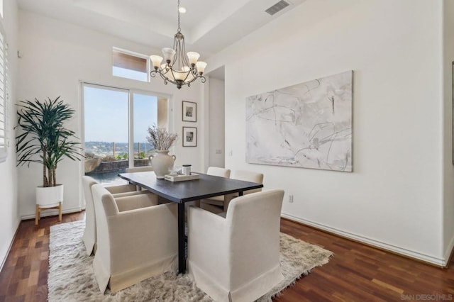 dining space with dark wood-type flooring, a chandelier, and a raised ceiling