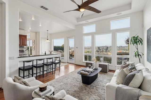 living room with ceiling fan, wood-type flooring, and a raised ceiling