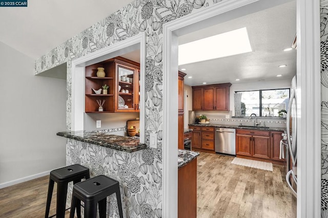 kitchen with a skylight, dishwasher, sink, a breakfast bar area, and dark stone counters