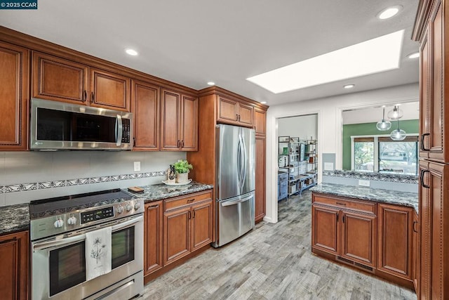 kitchen featuring appliances with stainless steel finishes, decorative light fixtures, light wood-type flooring, and dark stone counters