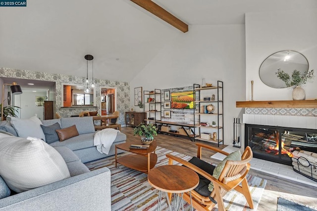 living room with a chandelier, high vaulted ceiling, beam ceiling, a tiled fireplace, and light hardwood / wood-style floors